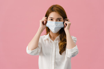 Young Asia girl wearing medical face mask with dressed in casual clothing and looking at camera isolated on pink background. Self-isolation, social distancing, quarantine for corona virus prevention.