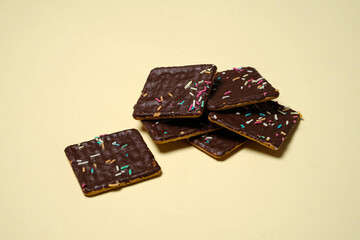 Stack of biscuits with chocolate topping sprinkled with colorful sprinkles isolated on yellow background. Delicious and crunchy biscuits. Biscuits are suitable to eat during your break time.