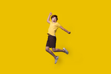 Ginger caucasian boy is jumping on a yellow studio wall with free space smiling at camera