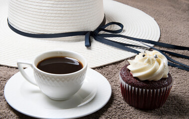 Cupcake on fabric background, white coffee cup, homemade cake with cream and women’s hat on table. Selective focus. - Powered by Adobe