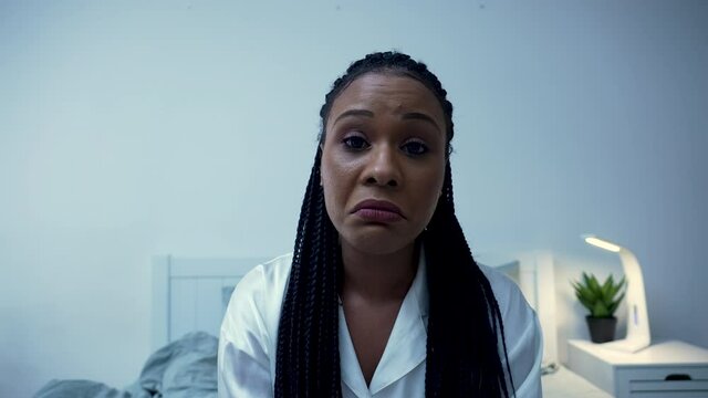 Pretty African American woman talks to someone on a video call, yawns bored and interrupts conversation by closing laptop. Black female posing in bedroom on bed in her pajamas. Close up. Slow motion.