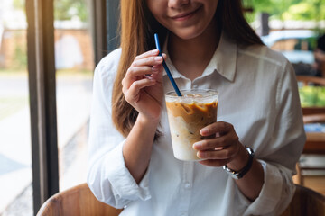 Closeup image of a beautiful young asian woman holding and drinking iced coffee