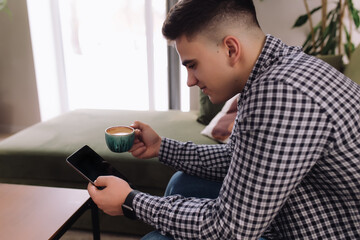 Smiling man reading smartphone, black screen and coffee cup. Blurred background