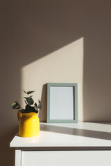 Yellow ceramic jug or vase with eucalyptus branches, empty white photo frames