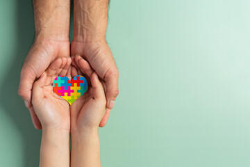 Adult and child hands holding jigsaw puzzle heart shape, World Autism Awareness Day