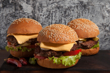 Group of burgers on a wooden board on a dark background, the backdrop is a concrete wall