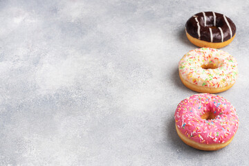 Assortment of donuts in icing on a gray concrete table, copy space.