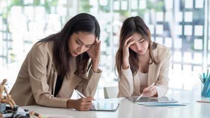 Two young asian businesswoman are stressed by working on a tablet at the office.