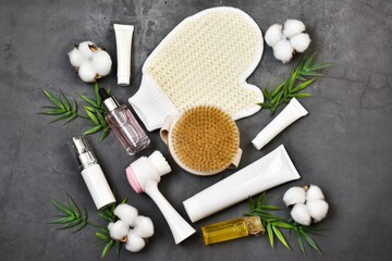 Natural spa cosmetics and cotton accessories. Facial brush, massage brush, tubes on a gray concrete background with cotton flowers. Copy space. Flat lay.