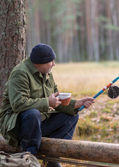 Naklejka premium fisherman by the river sits on a tree branch and drinks tea, blurred tree background, autumn