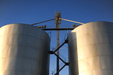 Close-up view of two large grain silos with central access stairway and conveyors, representing agricultural storage systems and vertical integration in food supply logistics