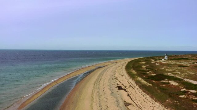 Aerial shot of lighthouse at beach against blue sky on sunny day, drone flying forward over coastline - Cape Cod, Massachusetts