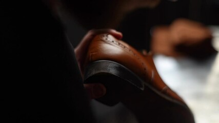 Close-up back view of shoemaker painting heel and sole of light brown leather shoes with brush during restoration working. Process of repairing and restoration shoes by cobbler in shoe repair shop.