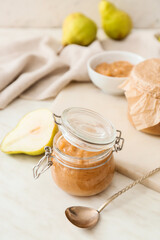 Jar of tasty pear jam on light background