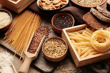 Different cereals, raw pasta and bread on wooden background, closeup