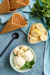 Bowl with tasty banana ice-cream and waffle cones on color background