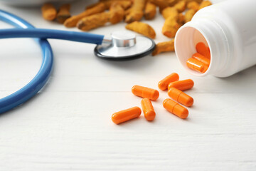 Bottle of turmeric pills and stethoscope on light wooden background