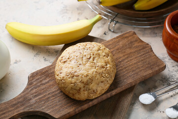 Board with fresh dough and banana on light background