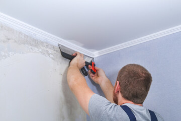 A man glues gray vinyl wallpaper on a non-woven backing. Renovation of the room.