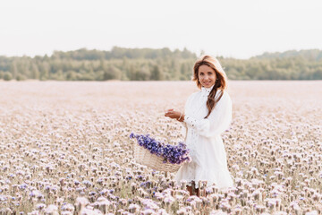 Fototapeta na wymiar girl in a white dress with a bouquet of flowers in a basket in a field
