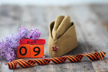 Wooden calendar with Russian text May 9, garrison cap, george ribbon and a bouquet of lilacs on a...