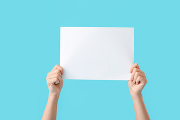 Female hands with empty paper sheet on color background