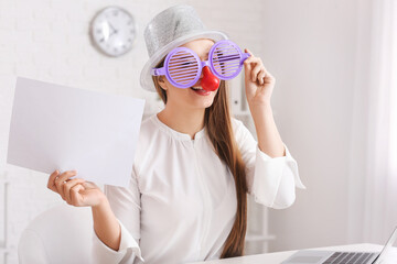 Young businesswoman in funny disguise and with empty paper sheet sitting at workplace in office....