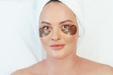 Portrait of a woman lying in a spa beauty salon with eye patches applied and with towel on her head