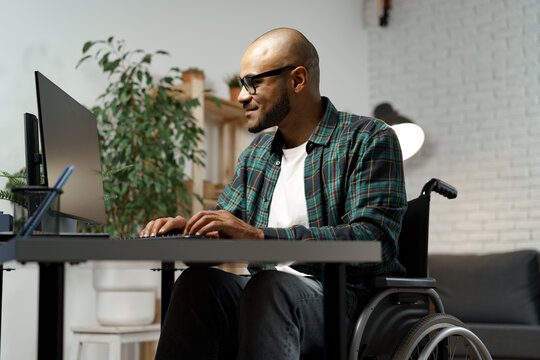 Disabled young african american man in wheelchair using computer while sitting at his working table