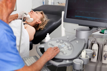 Naklejka premium Elderly diligent efficient friendly man sonographer using ultrasonography machine checking female patient in hospital diagnostic room