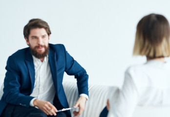A man in a classic suit sits on the couch indoors with documents and a woman vacancies