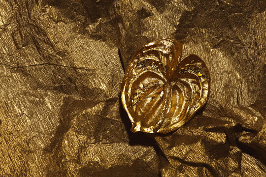 Modern stylish decor concept. Golden anthurium flower on golden wrpping paper background. Flat lay. Copy-space. Close up. Studio shot