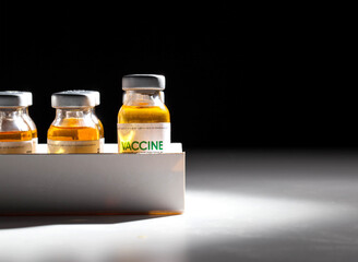 Vials with coronavirus vaccine in packaging on a black background and illuminated by a beam of light. Population vaccination recipe, vaccine research, SARS-Cov-2