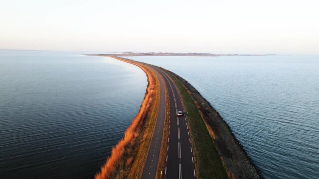 A car on an open road with water surrounding driving at sunset. The Netherlands near Marken.