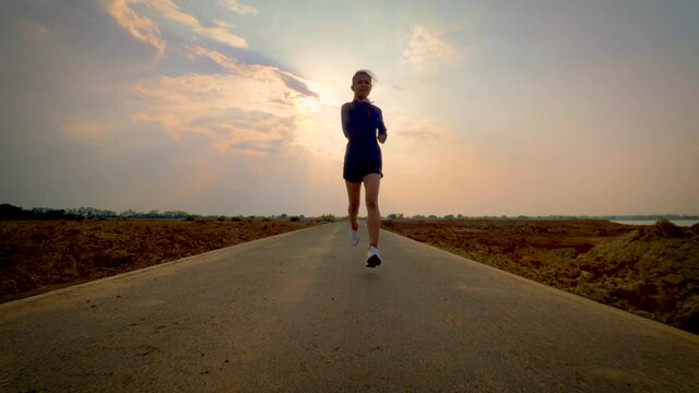 Young woman running sprinting on road. Fit runner fitness runner during outdoor workout with sunset background.