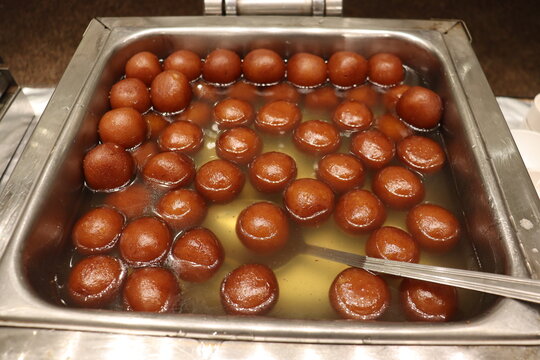 A large container full of delicious Indian sweet balls- Gulab Jamun and Rasgulla.