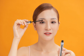 Closed-up of Asian woman is applying the mascara on yellow background