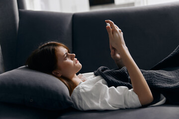 woman under the covers on the sofa and mobile phone in hand