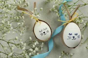 Easter bunnies made of eggs, ribbon and gypsophila flowers on white textured background