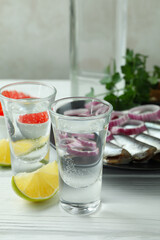 Shots of vodka and tasty snacks on white wooden background