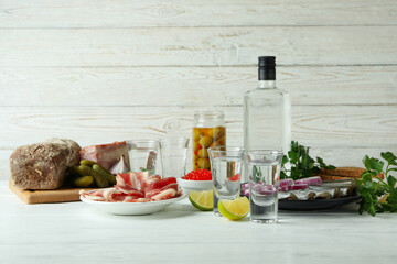 Shots of vodka and tasty snacks on white wooden background