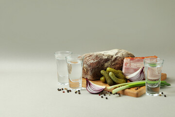 Shots of vodka and tasty snacks on light gray background