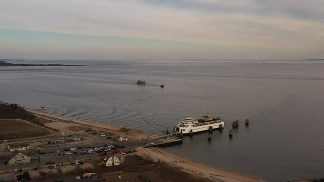 an aerial shot of an Orient Point ferry as it takes on vehicles and passengers. It was a cloudy day at sunset as the camera truck left, boom down and dolly out. A boat is being towed in the distance.