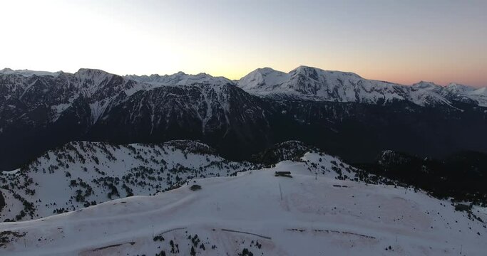 Chamrousse ski resort in the French Alps during sunrise with tracks below, Aerial pan left reveal shot