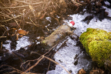 Used glass bottle, in the forest, in the spring under the melted snow. 