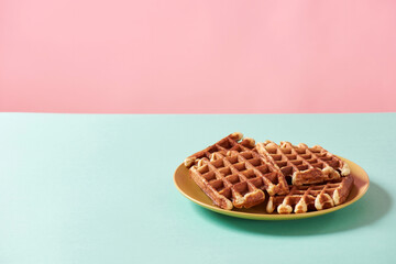 Belgian dessert. Freshly baked waffles with sugar on yellow plate isolated over blue and pink background