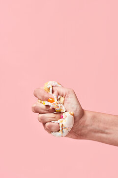 Hand squeezing donat against pink background, vertical shot