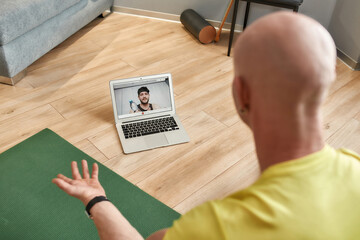 Fototapeta na wymiar Mature male fitness instructor explaining workout techniques online while having video conference, going to start virtual fitness class by webcam on laptop