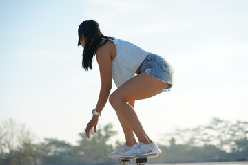  Asian women surf skate or skates board outdoors on beautiful summer day. Happy young women play surf skate at park on morning time.