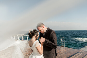 beautiful couple groom and bride are hugging on the pier against the backdrop of the sea and...